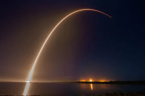 A rocket launch creates an arch of light across the night sky. The rocket is carrying Eutelsat satellites.