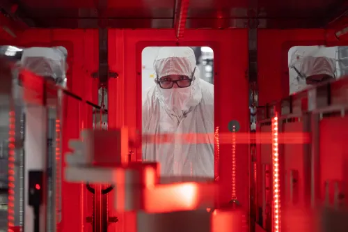 A man in full safety gear looks through a window at a chip being made at a Texas Instruments site
