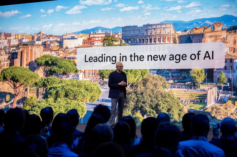 microsoft ceo satya nadella speaks to a crowd in front of a slide that says "leading in the new age of ai"