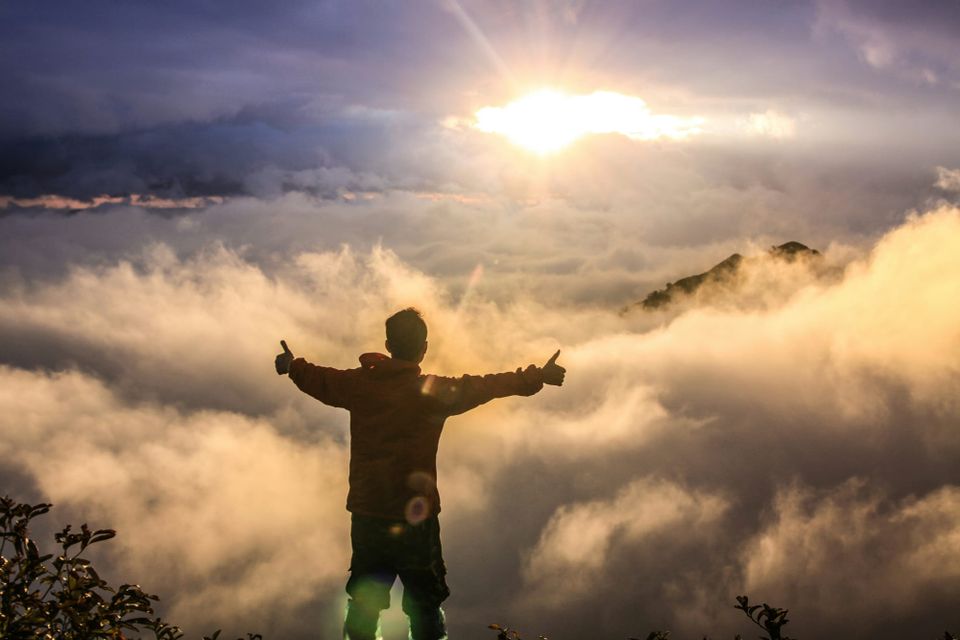 A man gives two thumbs up standing in front of clouds at the top of a mountain. FedRAMP will speed up its approval process for cloud providers
