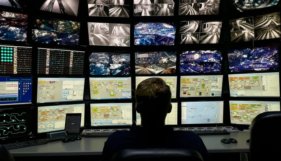 A man sits at a desk in front of a large bank of screens displaying camera footage and data. The UK Home Affairs Committee found local police needed more support on online surveillance