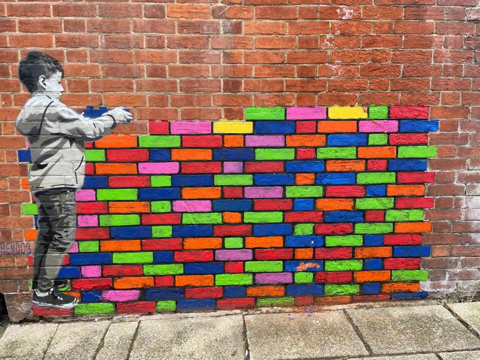 Graffiti on a wall shows a young boy stacking lego-like colourful bricks. LangChain's Open Agent Platform is an open source AI agent builder