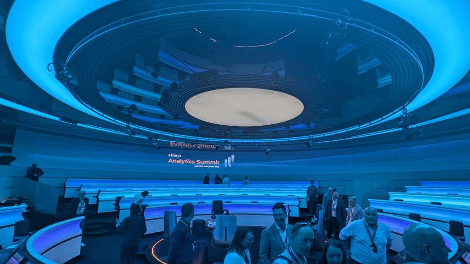 A conference room with the word "Alteryx Analytics Summit" on the wal
