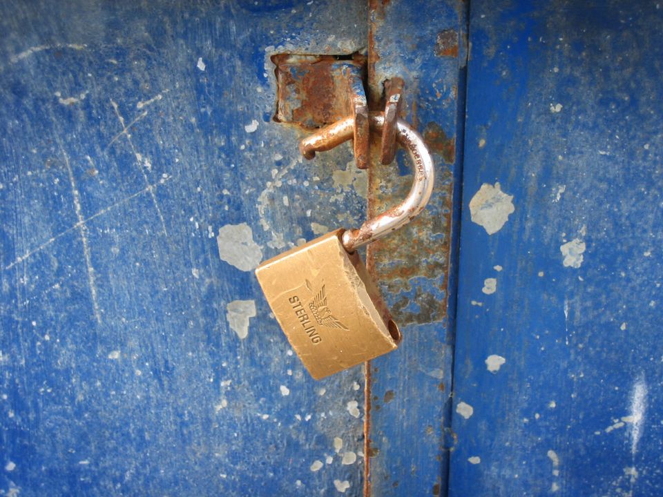 A unlocked padlock hanging from a rusty door. 