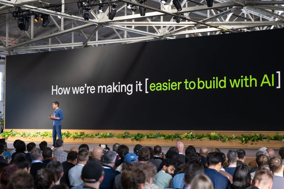 OpenAI CEO Sam Altman speaks onstage at the company's 2025 Demo Day in front of a sign that says "How we're making it [easier to build with AI]
