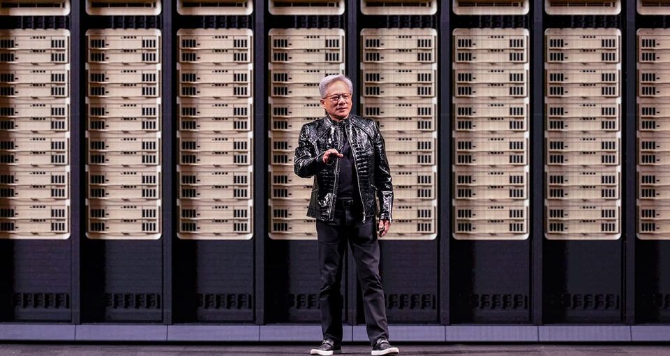 Nvidia CEO Jensen Huang speaking on stage wearing his trademark leather jacket in front of a picture of servers