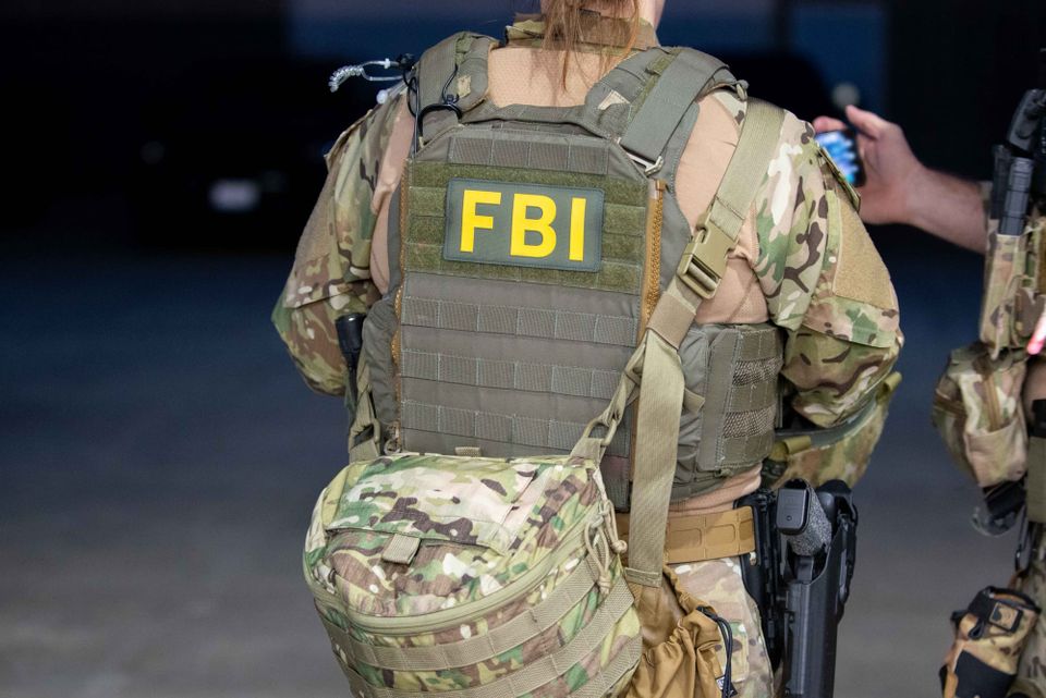 An FBI SWAT officer in army gear stands away from the camera with an FBI patch on their back.