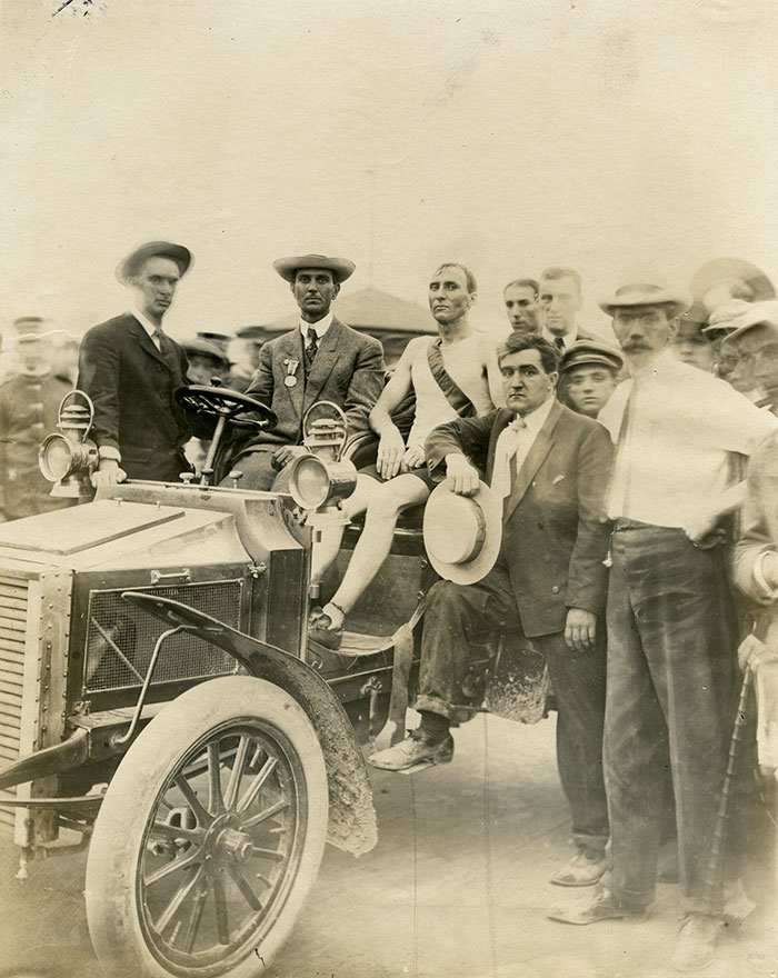 Thomas Hicks in a car, wearing a sash, surrounded by his team
