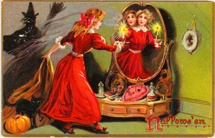 Antique postcard of a witch, black cat, pumpkin, and a woman staring into a mirror with a mysterious figure behind her. It says Hallowe'en in the lower right corner