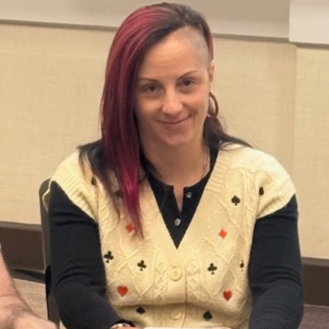 CK smiles at the table during the 2025 WSOP Monster Stack, wearing a cream-colored cardigan adorned with black and red playing card suit symbols.