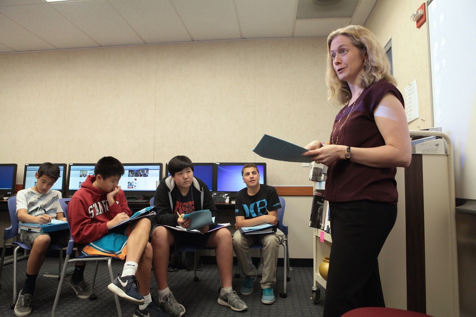 Guest teacher Sarah Cooper is standing, facing four students who are looking at her and sitting. 