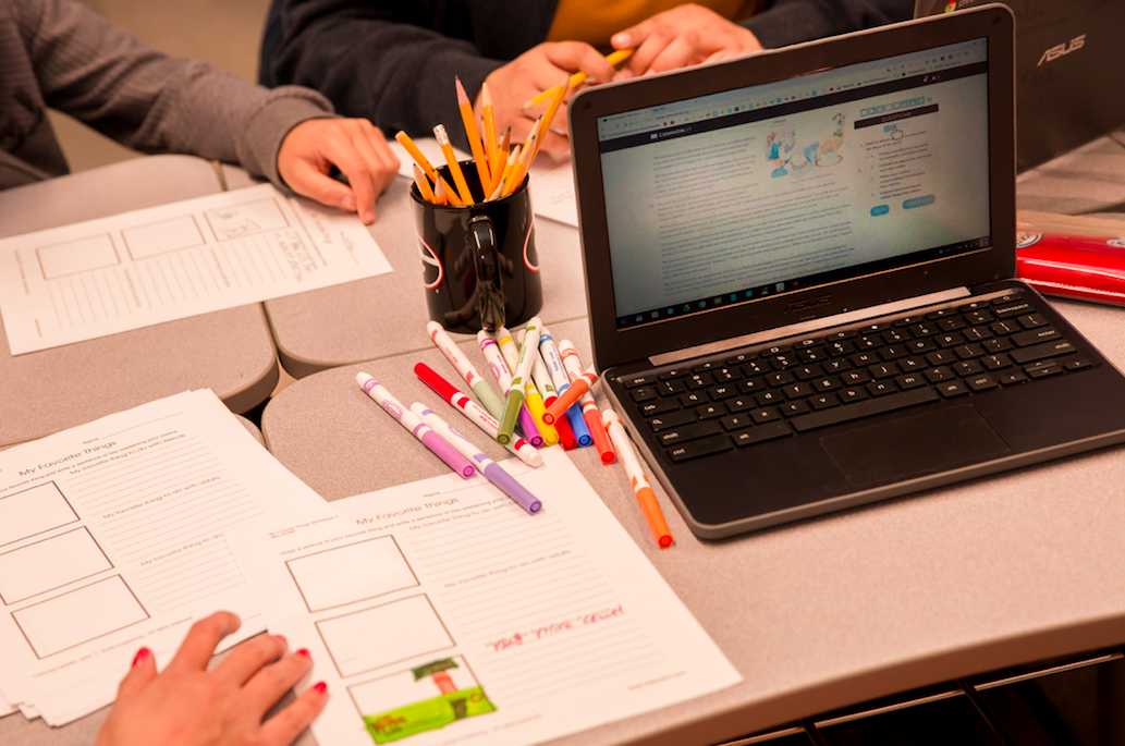 A student's desk with paper, markers, and open laptop.