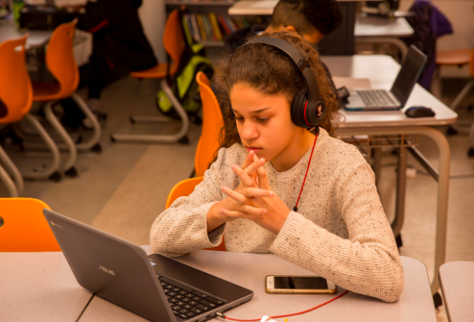 A student wearing headphones and looking down at her laptop.