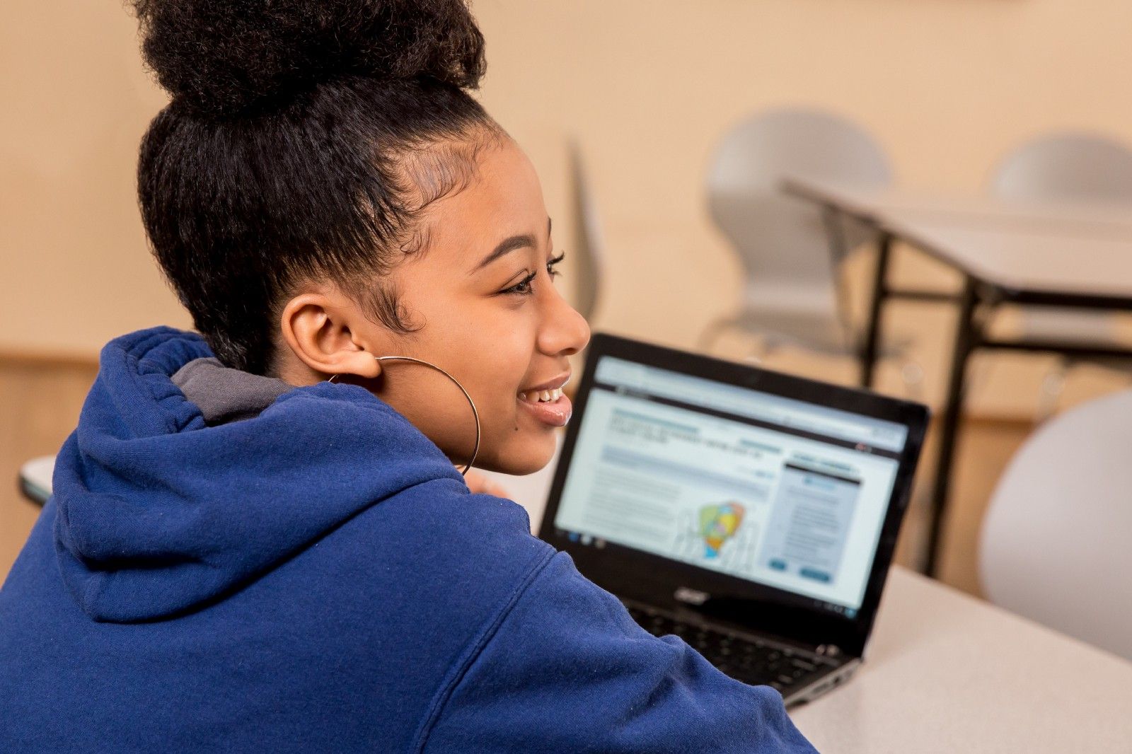 A student sitting at a table in front of a CommonLit lesson, looking away and smiling. 