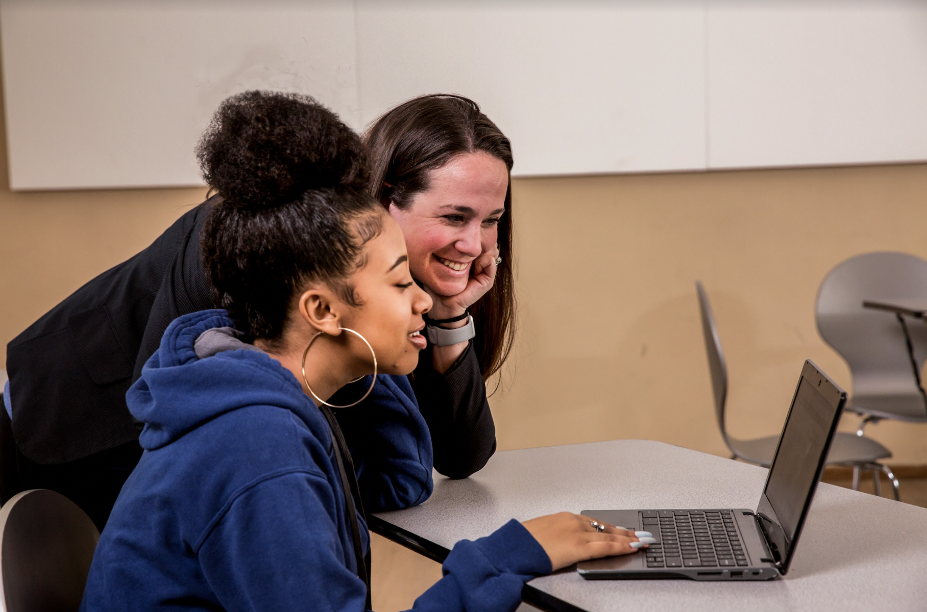 A teacher and student looking at a computer and smiling. 