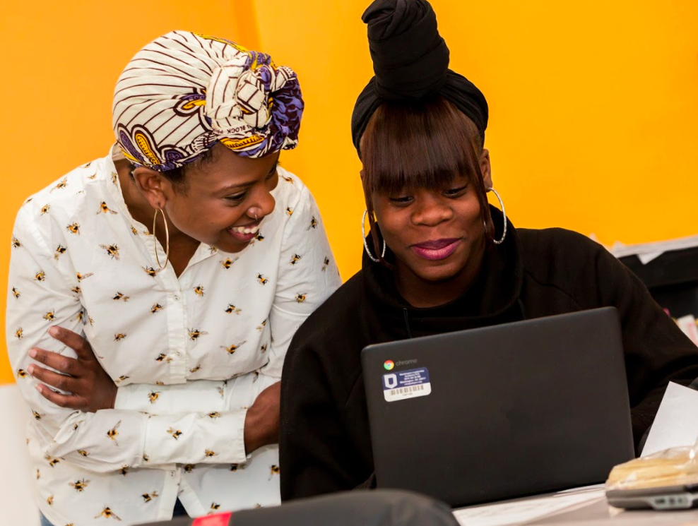 A teacher and student next to each other, smiling and looking at a computer screen.