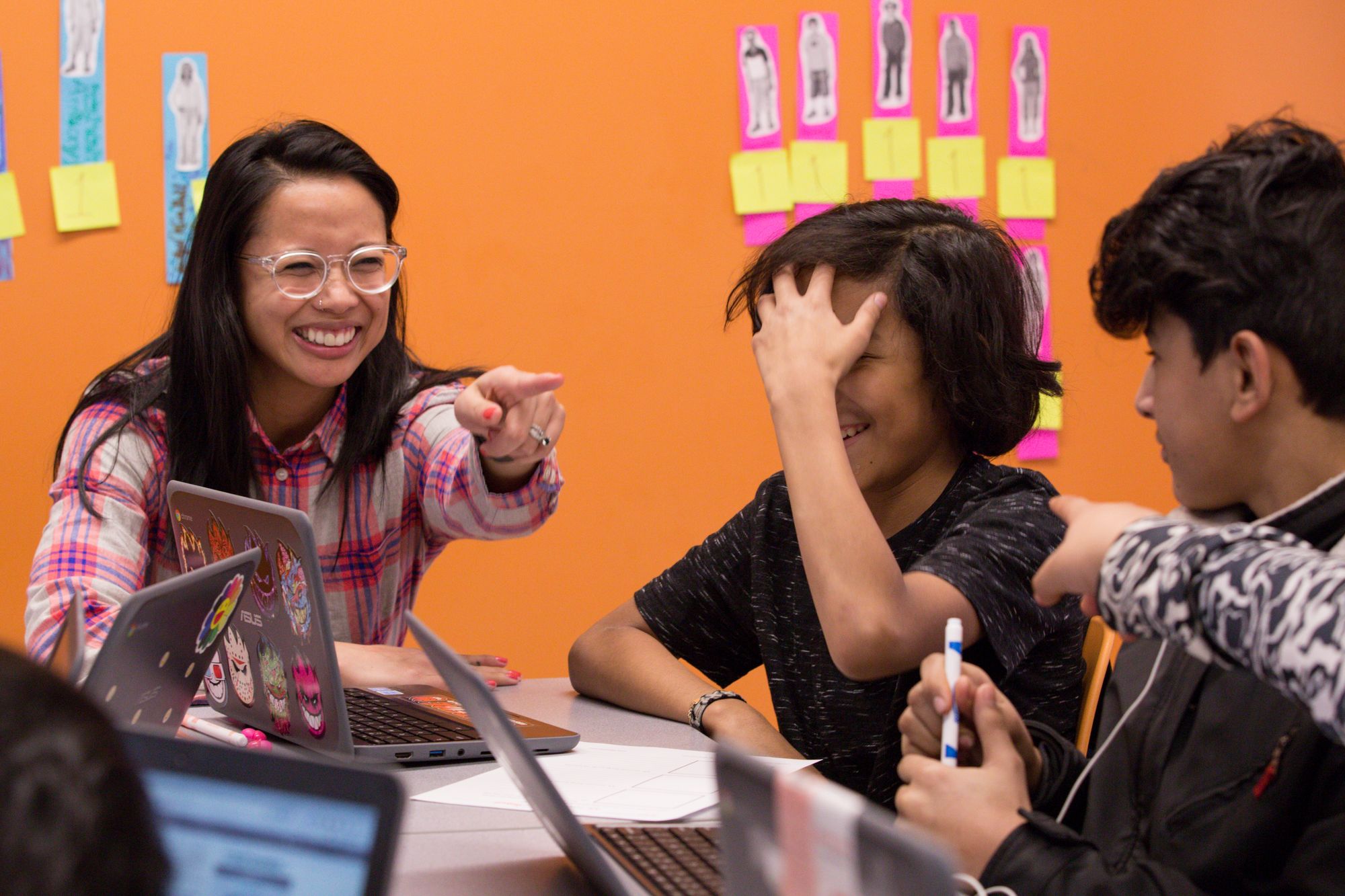 Teacher and students laugh while teacher points towards student. 