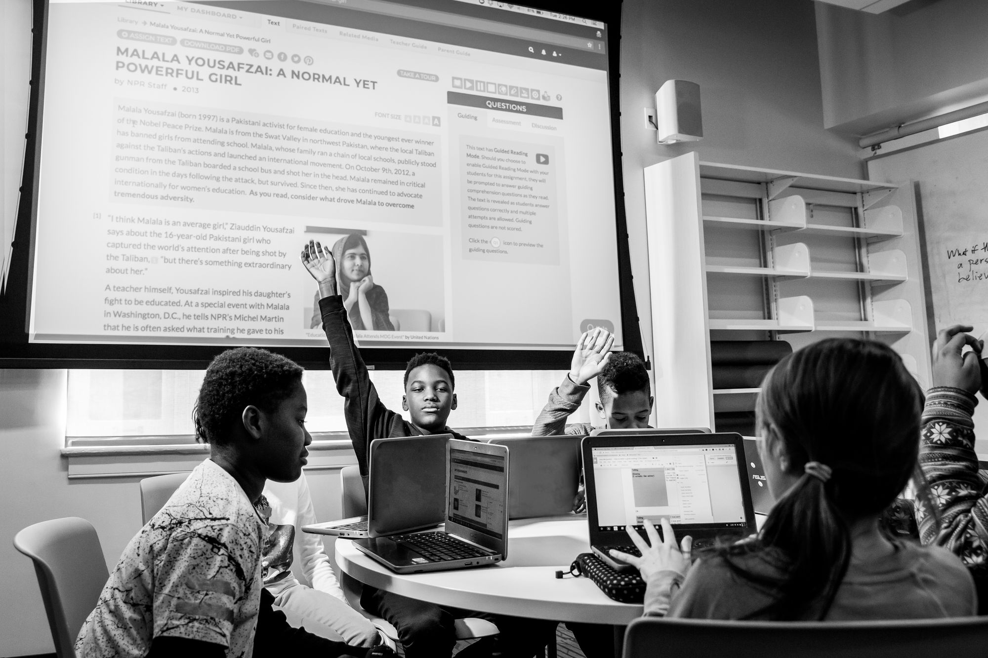Students on their laptops, raising their hands.