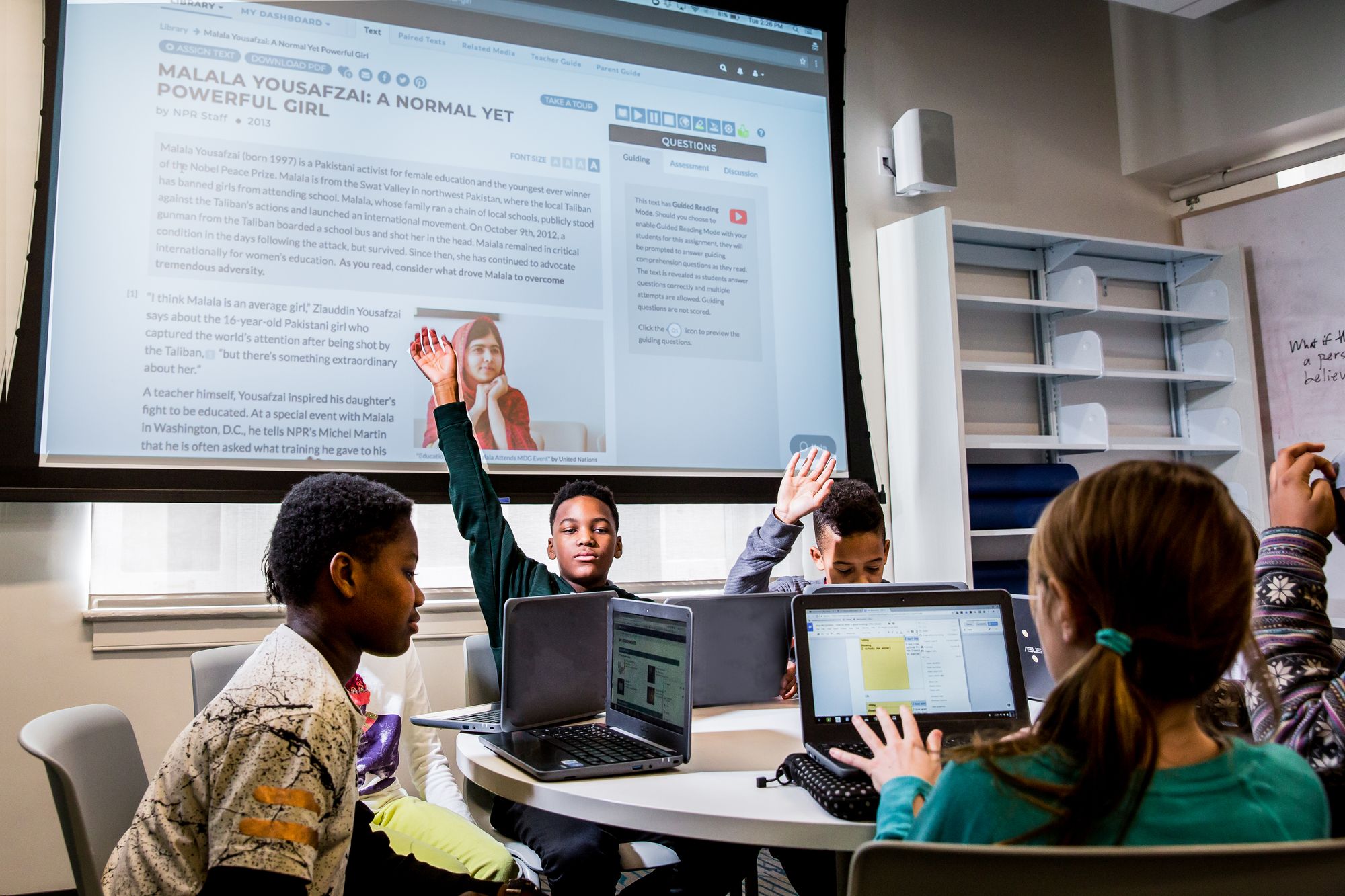 Student raises hand during round table discussion on poems about community. 