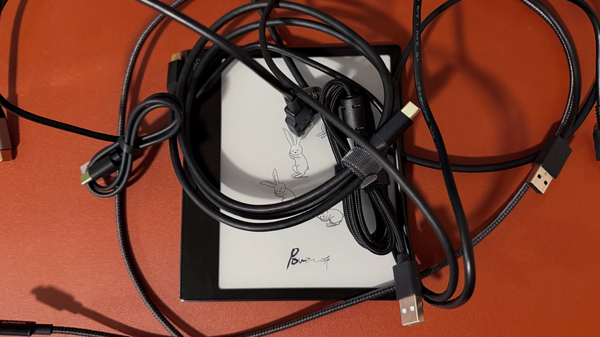 An ereader covered by a pile of usb cables.