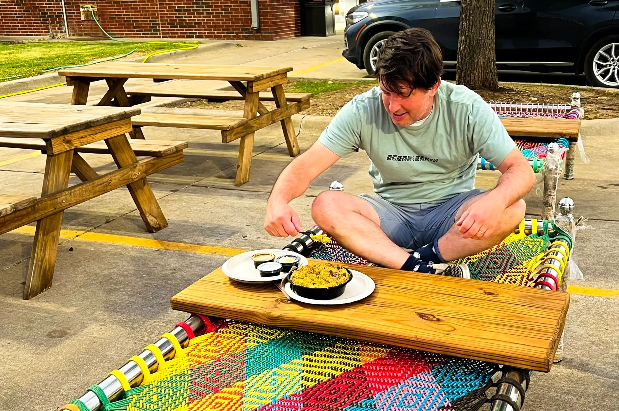 Author Rob Curran sitting cross-legged on a colorful webbed platform eating a bowl of biryani.