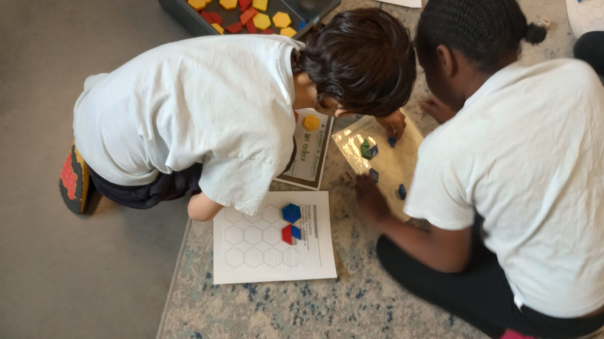 Two boys sit on the floor, bent over while working with pieces of plastic to build hexagons.