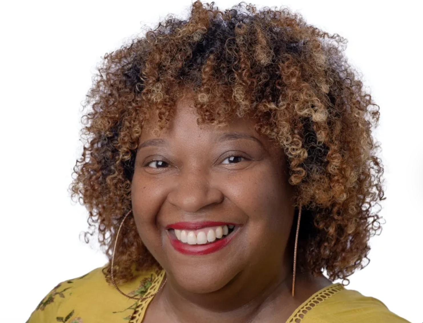 The photo shows a smiling woman with tight natural curls and hoop earrings, wearing a dark yellow shirt.