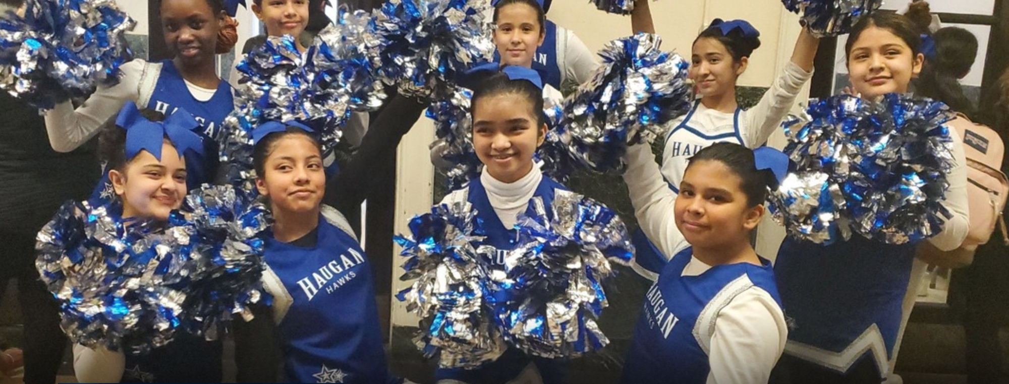 Eight girls in blue and white cheer outfits hold blue, white and silver pom-poms.