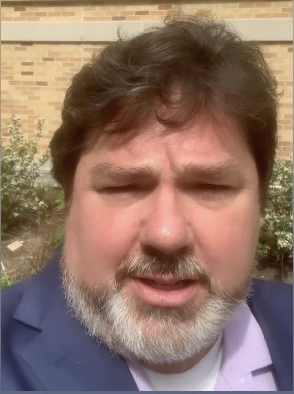 The photo shows a white man with brown hair and a graying beard.