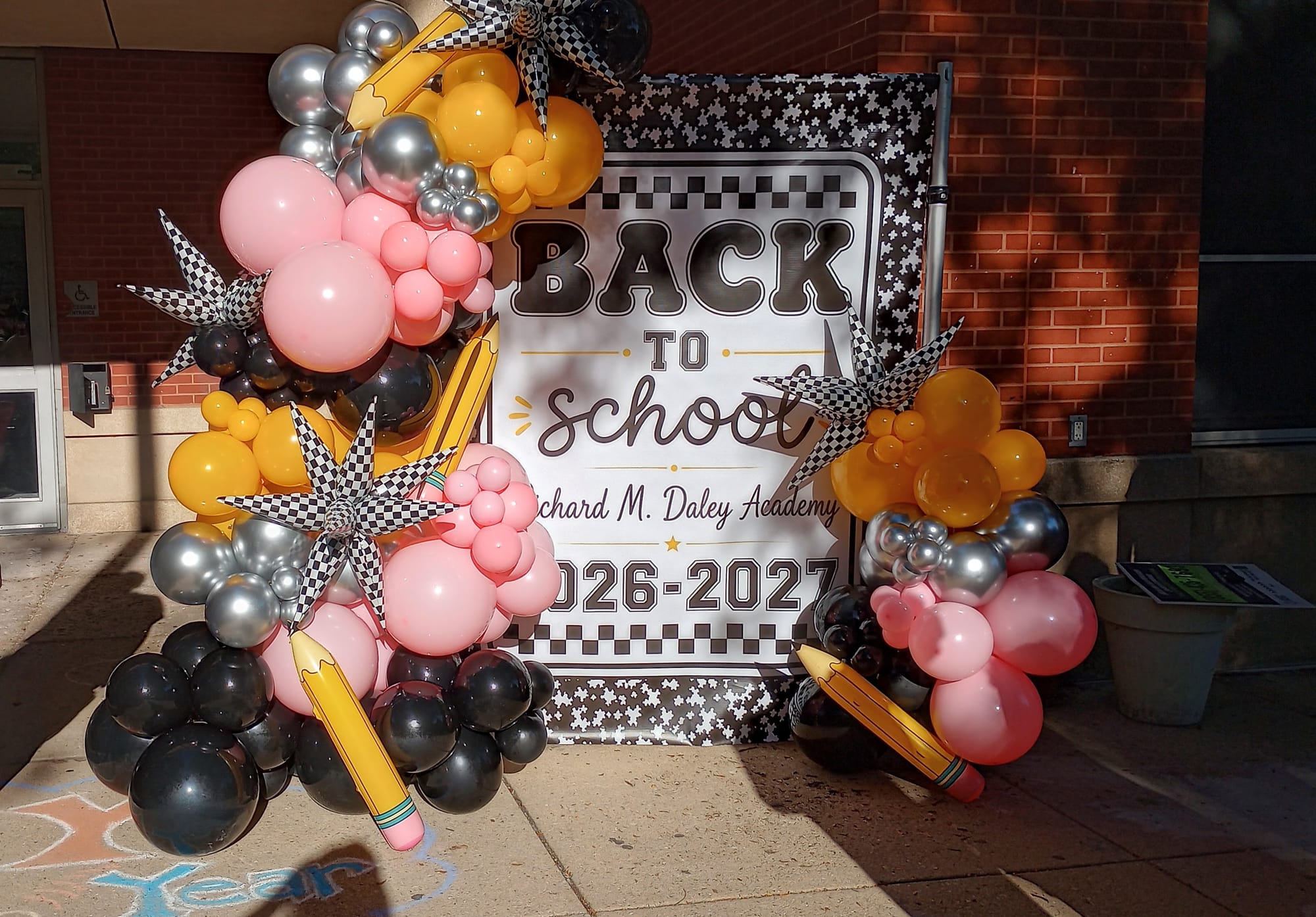 Balloons surround a giant composition notebook frame that reads: Back to School, Richard M.Daley Academy, 2026-2027.
