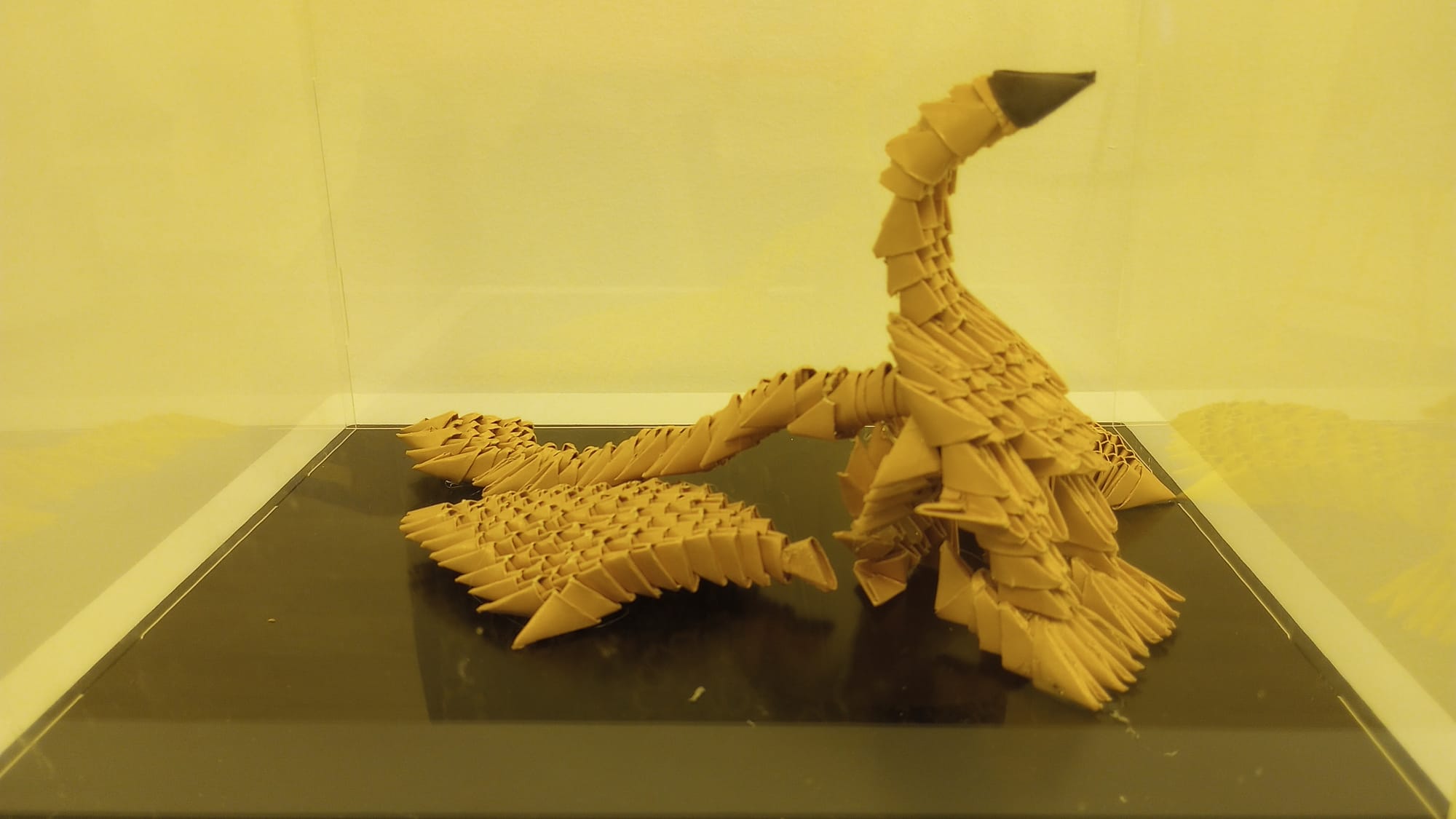The image shows a phoenix made of folded triangles, all of which are beige except for the dark brown beak at the top.