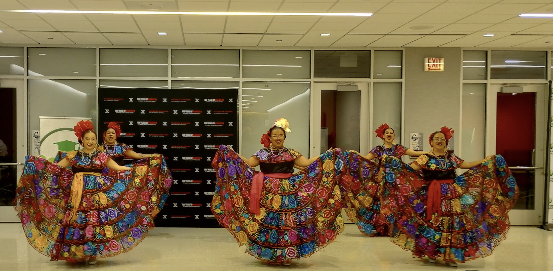 Six women in colorful Mexican dresses hold up their full skirts at the end of a dance.
