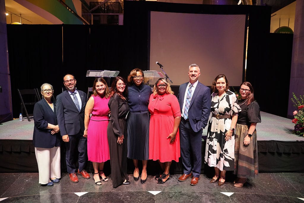 Nine people stand in front of a stage.