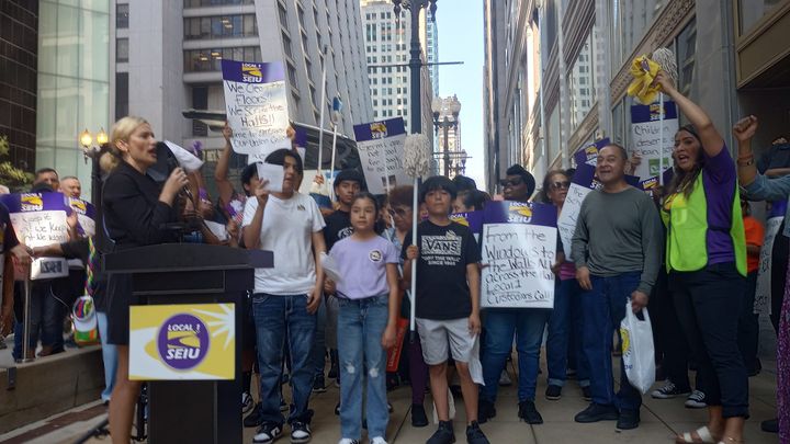 People hold mops and signs in front of the Chicago Public Schools's downtown headquarters to protest layoffs.