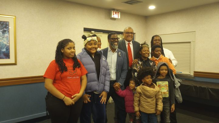 The photo shows board member Che "Rhymfest Smith" and Acting Chief Education Officer Alfonso Carmona in the center of a group of students and parent