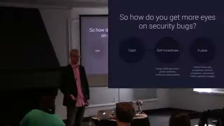 Casey Ellis on stage at SOURCE Boston 2014, next to a slide asking "So how do you get more eyes on security bugs?"