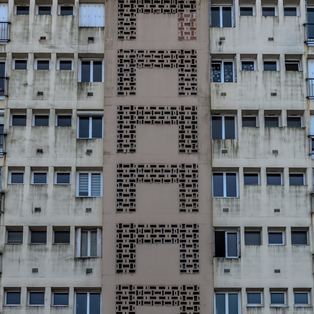 Façade d'immeuble à Quimper, avec une colonne centrale de claustras géométriques perforant le béton gris
