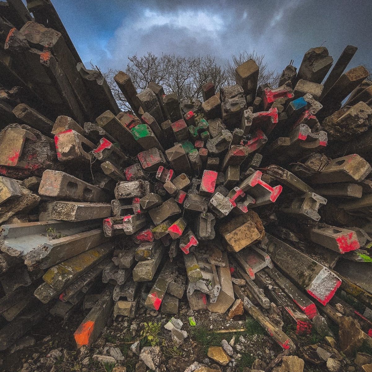 Poteaux électriques couchés et empilés, marqués de plastique rouge et rose, paysage rural du Finistère