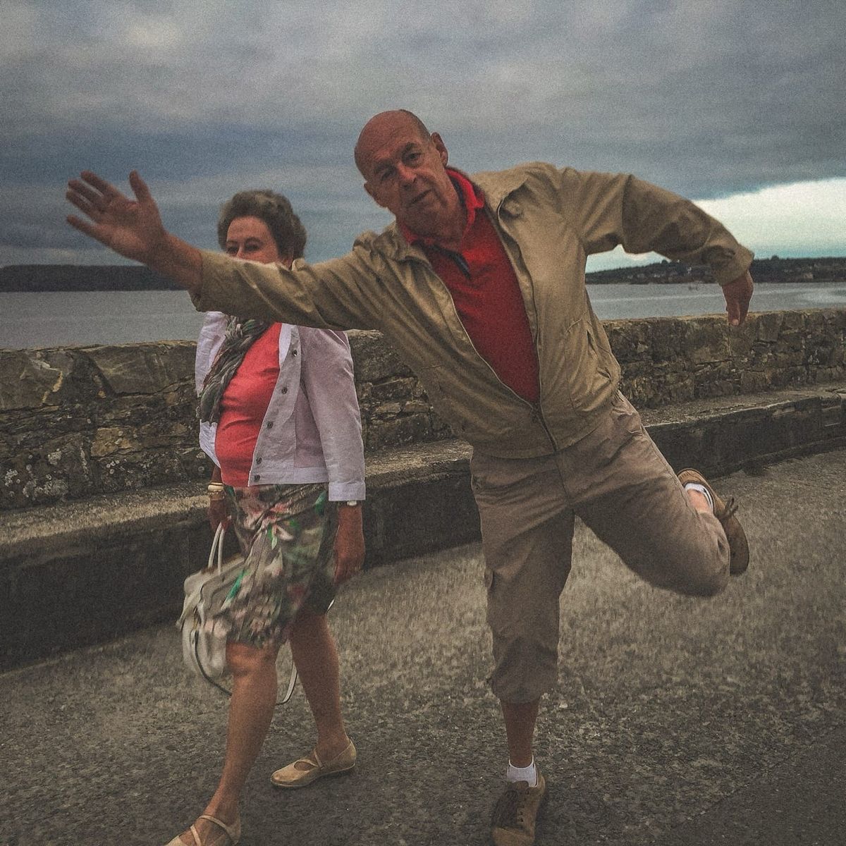 Homme levant le bras en entrant dans le cadre sur un quai à Camaret-sur-Mer, femme en arrière-plan