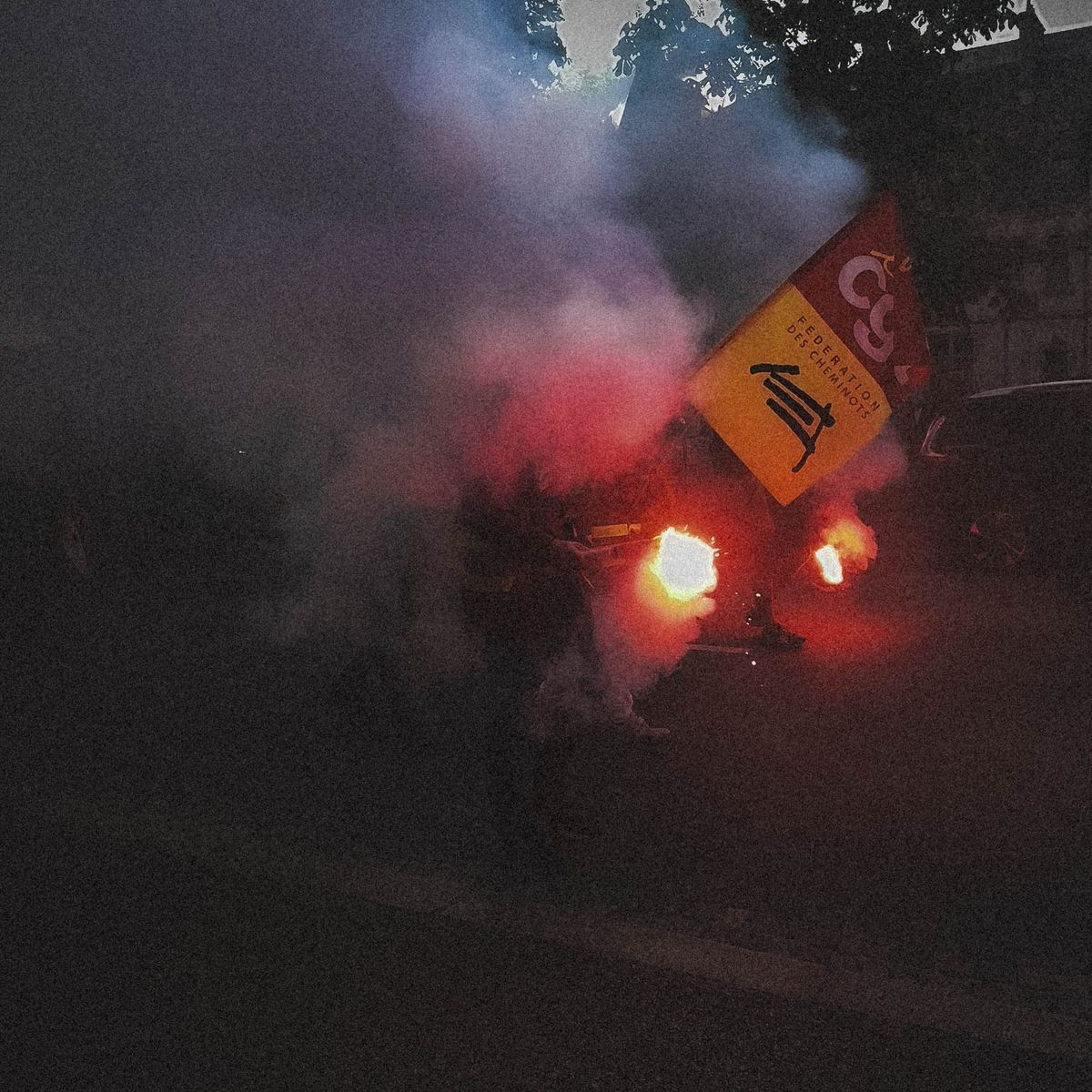 Fumigènes rouges et drapeau CGT des cheminots dans une manifestation du 1er mai à Quimper, scène noyée dans la fumée