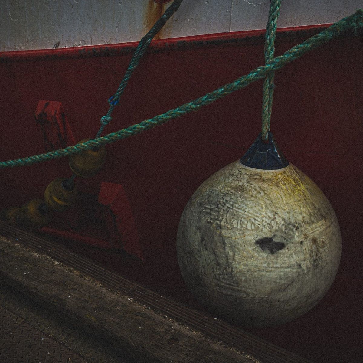 Bouée usée suspendue par un cordage dans le port du Guilvinec, coque rouge et traces d’usure visibles