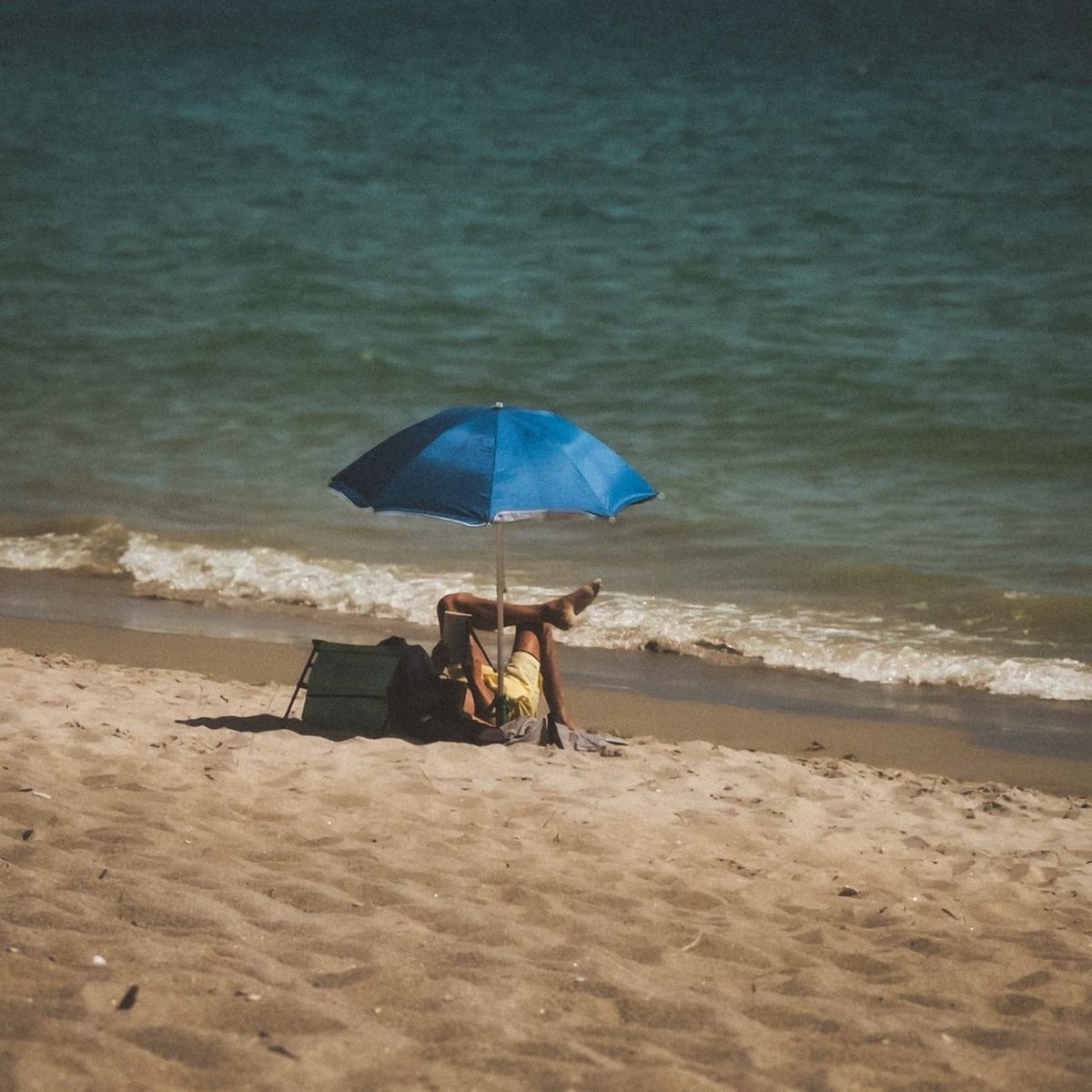Un homme lit sous un parasol bleu face à la mer sur la plage de Kermor à Combrit, dans le Finistère.