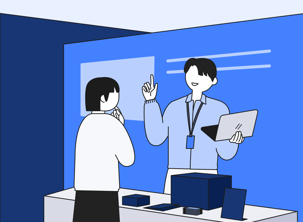 박람회 부스에서 스태프가 노트북을 들고 방문객을 응대하고 있다.