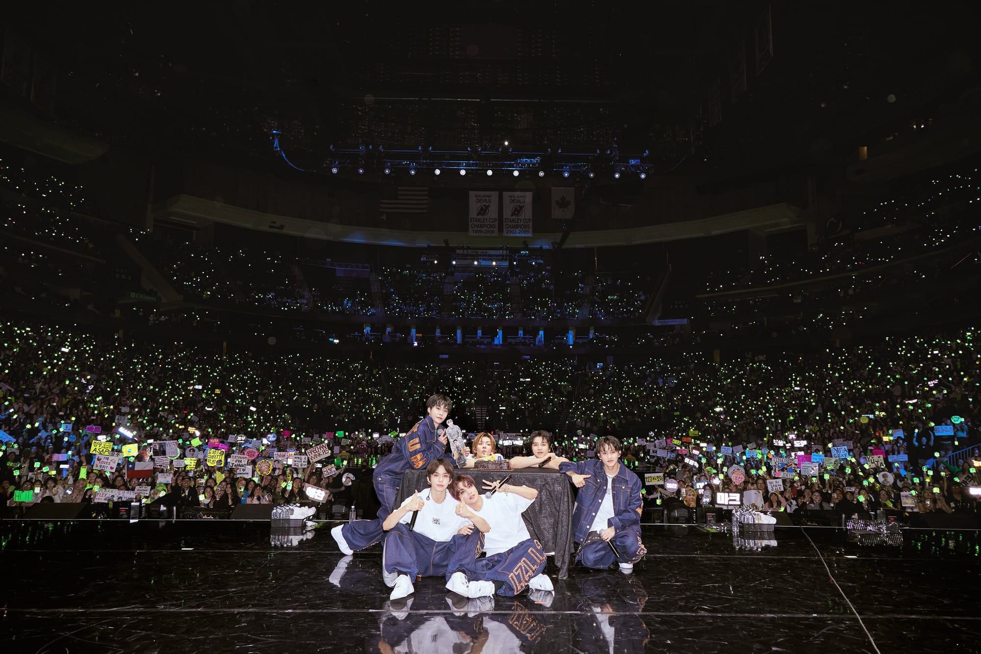 NCT 127 posing next to a cake in front of a crowded concert arena 