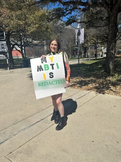 Woman holding sign that says "My MBTI IS" with a blur effect over a word and added text saying "REDACTED"