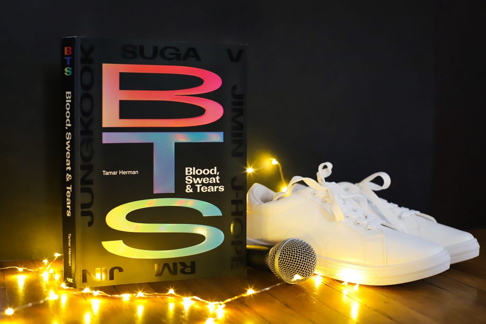 The book BTS: Blood, Sweat & Tears on a stage with sparkling lights, a mic, and sneakers
