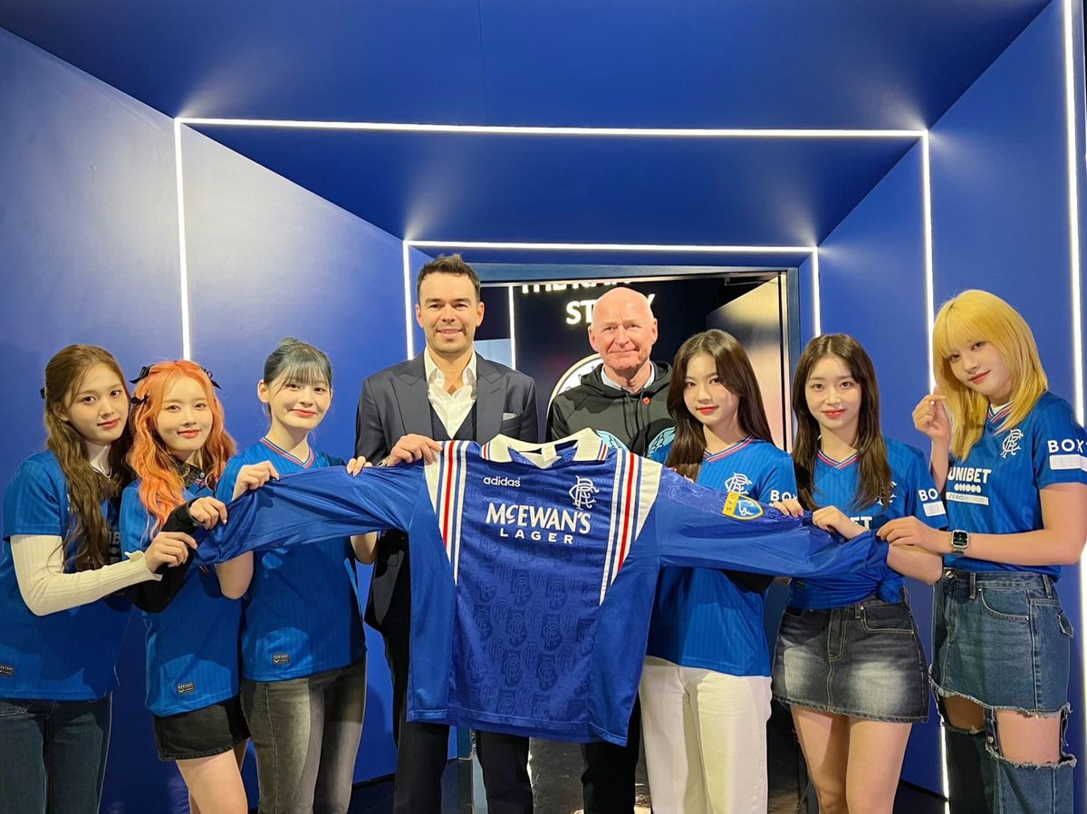 StayC wearing jersies while holding a jersey with two white guys, ostensibly the owner/manager/coach/etc. of the Rangers