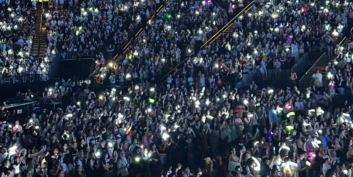 A crowd of fans with lightsticks lit up, predominantly in white but with different pockets of color as well.