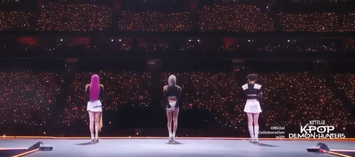 BabyMonster facing away from the camera on-stage, performing K-Pop Demon Hunters at MAMA with the words "Official Collaboration with NETFLIX K-POP DEMON HUNTERS"