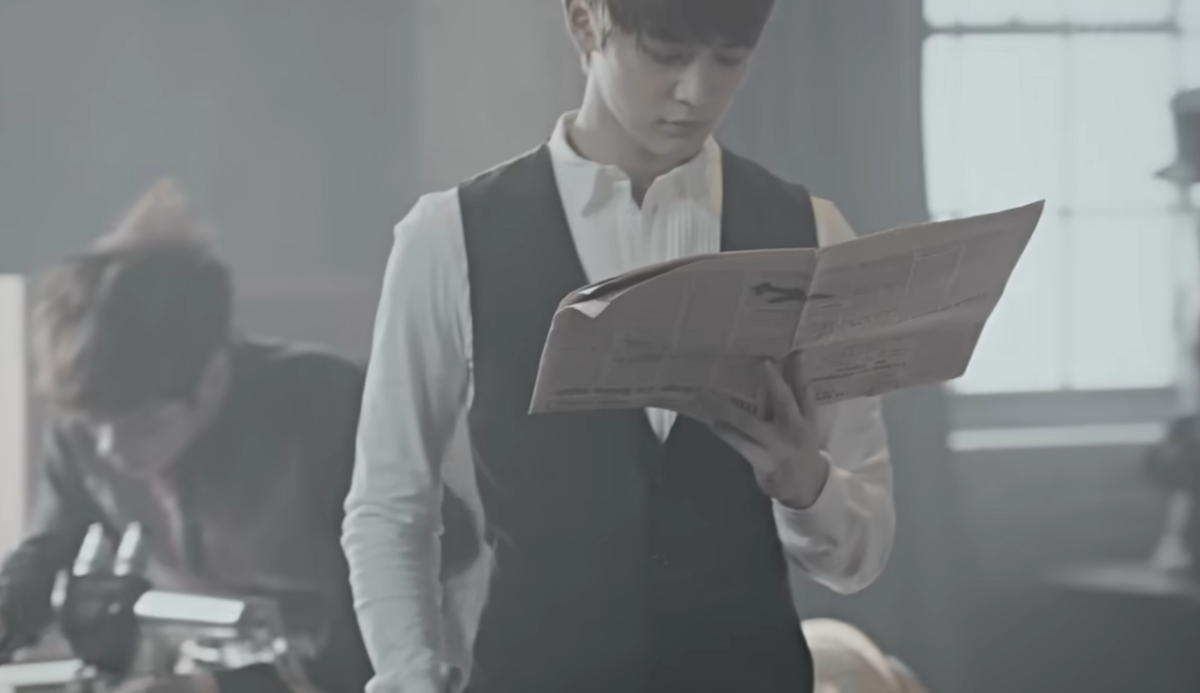 A man reading a newspaper, a man behind him looking at a microscope 
